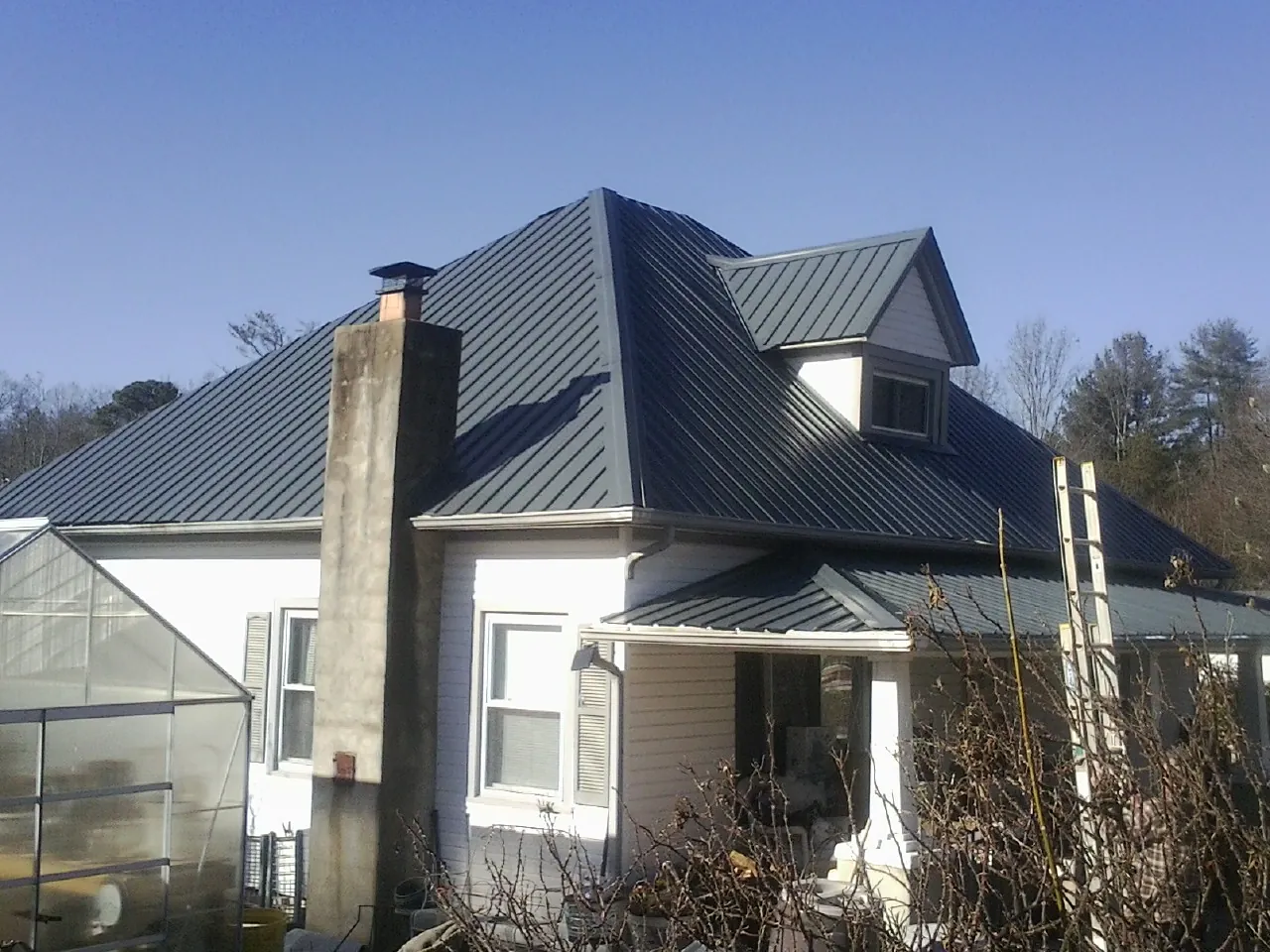 Dark blue standing seam metal roof on a white farmhouse with dormer — Slate & Tile Roof Repair by Roofing Brothers in Port Townsend