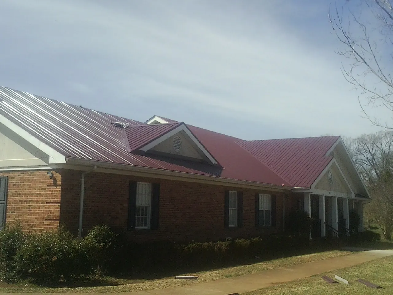 Red metal roof with gabled entries on a long brick building, from a Hail Damage Roof Repair job in Port Townsend