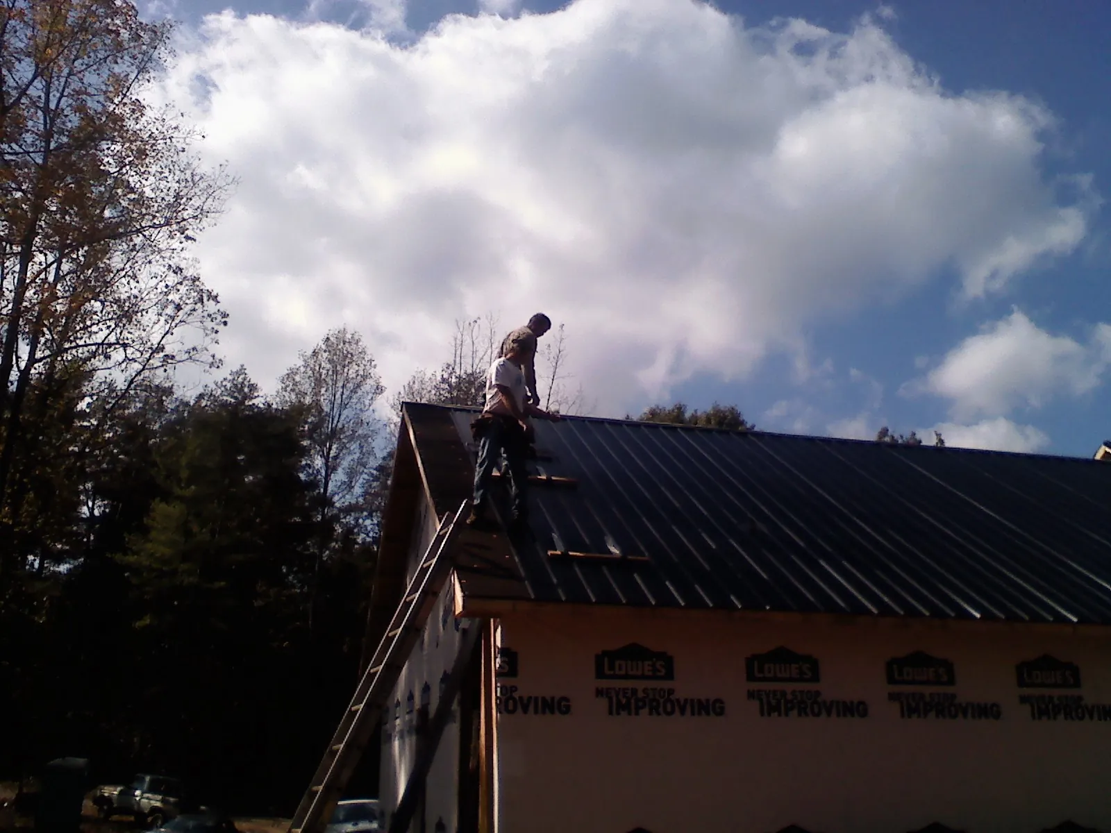 Roofer fastening dark metal panels high against a cloudy sky, from a Roof Inspection job in Port Townsend
