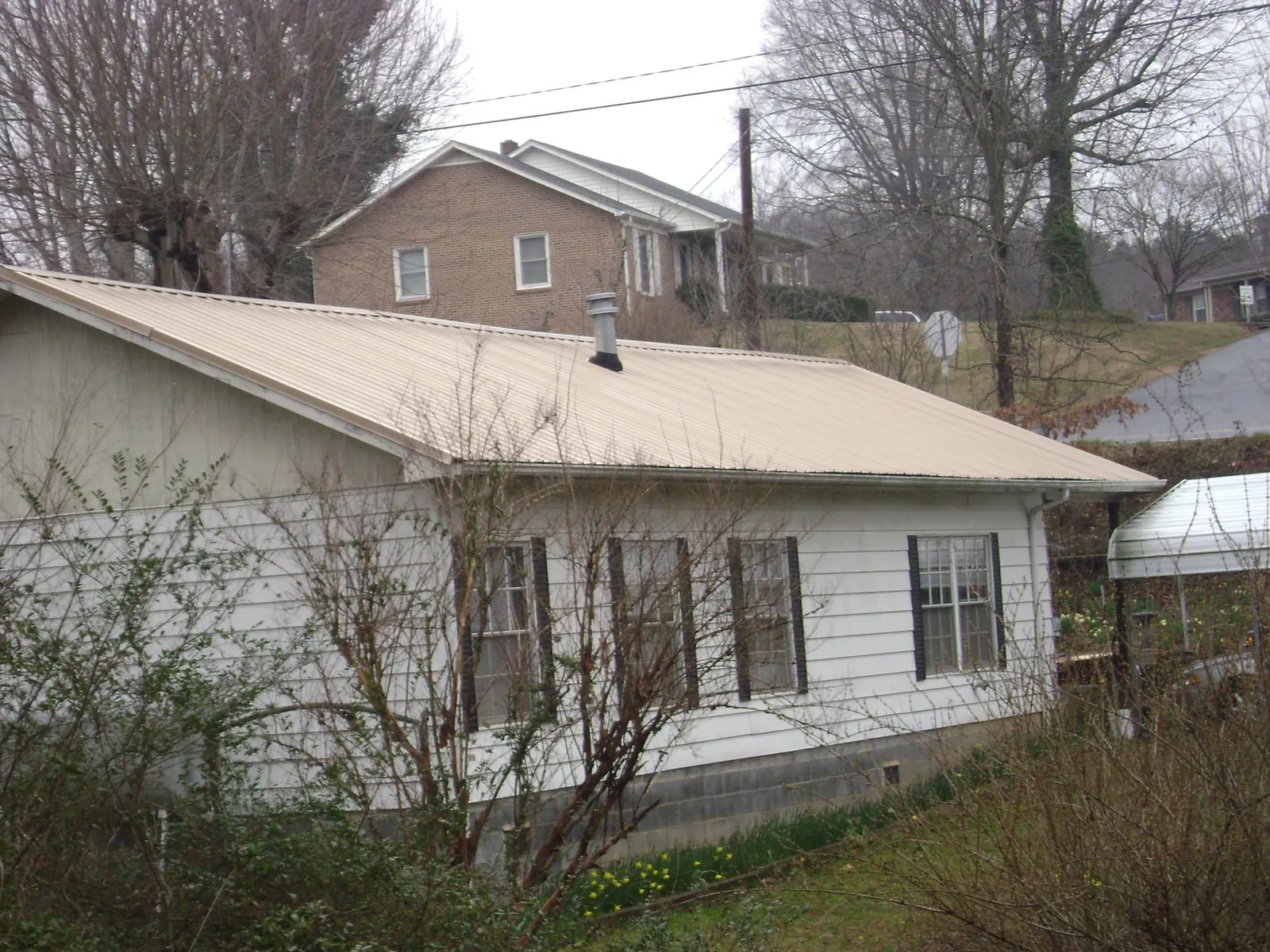 Tan metal roof on a white sided house set into a hillside — Commercial Roofing by Roofing Brothers in Port Townsend